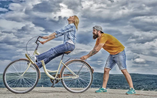 Man helps keep balance and ride bike. How to learn to ride bike as adult. Girl cycling while boyfriend support her. Woman rides bicycle sky background. Cycling technique. Learn cycling with support