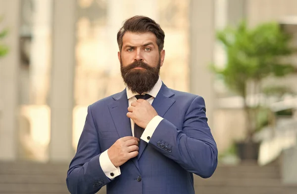 Προσαρμόστε το σύνολο σας με γραβάτα. Ο γενειοφόρος άντρας φτιάχνει τη γραβάτα φορώντας μπλε κοστούμι στην ύπαιθρο. Κλασικό στυλ μόδας. Κομψό επίσημο ένδυμα Τυπική μόδα. Ανδρικά ρούχα. Επαγγελματικό ντύσιμο. Προσοχή στη λεπτομέρεια — Φωτογραφία Αρχείου
