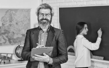 Sakallı adam not defterine not alır. Küçük kız tahtaya cevap yazmış. Sınav ya da ders. Okula dönüyorum. Modern eğitim konsepti. Öğretmen ve çocuk sınıfta. görev değişikliği