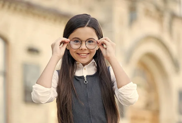 Criança feliz em uniforme escolar colocar óculos de moda para ver bem ao ar livre, visão — Fotografia de Stock