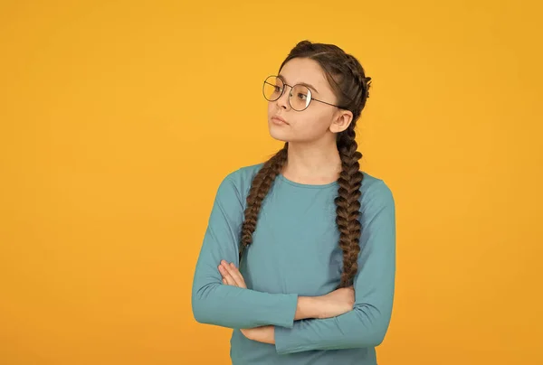 Glückliches Teenie-Mädchen mit geflochtenem Haar trägt eine Brille zur Sehkorrektur auf gelbem Hintergrund, smart — Stockfoto