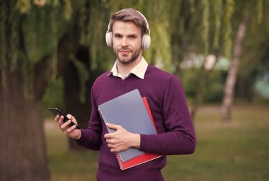 E-postalarına bak. Adam kulaklıkla müzik dinliyor ve not defterini tutuyor. Kulaklıklı yakışıklı adam parkta dinleniyor. Telefonu kullanıyor. Modern yaşam eğitimi teknolojisi. Öğrenci kitaptan bilgi alıyor. çevrimiçi çalış