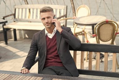 Resmi tarz konuşma işinde yakışıklı bir yönetici cep telefonu iletişiminde açık kafede dinleniyor, konuşuyor.