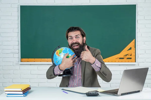 back to school. informal education. happy mature teacher hold globe and show thumb up. bearded man geographer work in classroom with map. prepare for exam. college lecturer on geography lesson