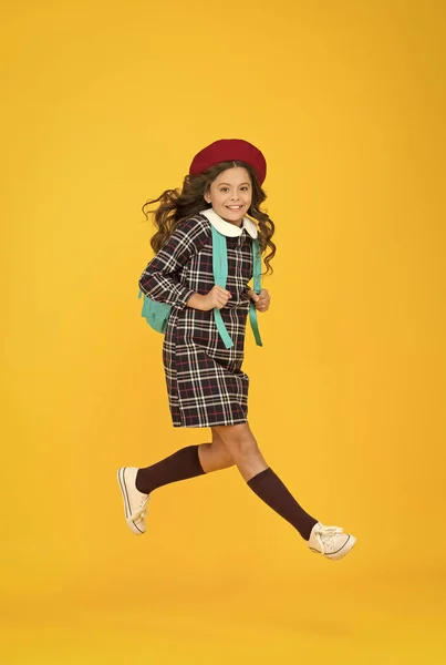 时髦的青少年大学生跳楼。背着背包上学的小女孩。教育概念。学校和时尚。穿着学生服的孩子。穿着法式贝雷帽，背景是黄色的。快点，快点 — 图库照片