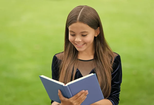 Glückliches Grundschulkind liest Bibliotheksbuch im Gras Sommer im Freien, zurück in die Schule — Stockfoto