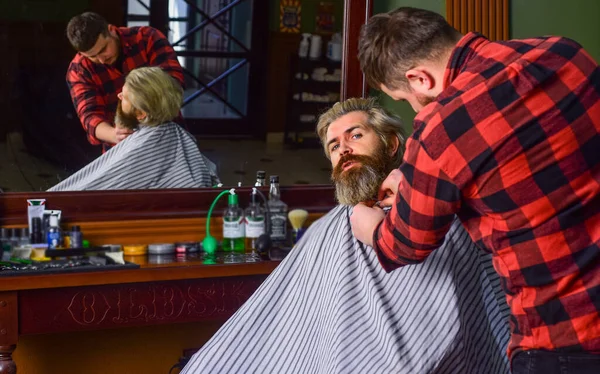 Sakallı adam. Berber dükkanı kavramı. Genç hippi sakallı adam berber dükkanında saçını kesiyor. Profesyonel kuaförlük işi. Yaşam tarzı. Usta berber saç stilini ve saç stilini kurutma makinesiyle yapıyor. — Stok fotoğraf
