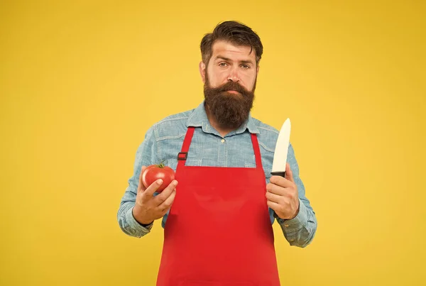 Hombre barbudo cocinar tomate rojo fresco con cuchillo afilado fondo amarillo, cocina —  Fotos de Stock