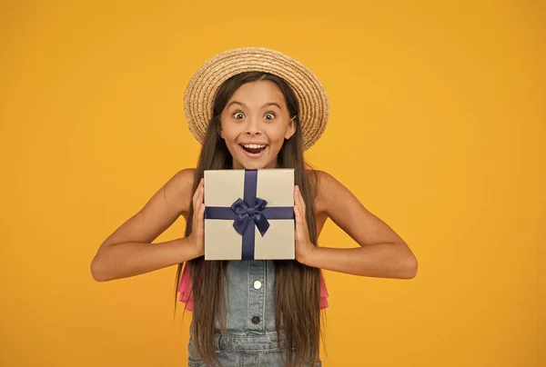 Itt a meglepetés ideje. Boldog lány tartsa ajándék sárga háttér. Meglepetés doboz. Meglepett a kisgyerek tekintete. Születésnapi meglepetés. Szuvenír. Ünnepnap. Boksz nap. Ünnepi meglepetés. Csomagold be. — Stock Fotó