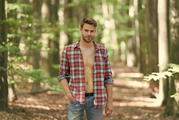 Sexy Macho im aufgeknöpften Hemd. Der junge unrasierte Mann hat einen nackten Oberkörper. männliche Schönheit und Mode. Typen mit Borsten tragen kariertes Hemd. casual fashion style. muskulöser Mann im Wald — Stockfoto