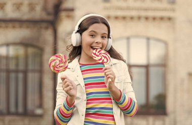 Neşeli kız modern kablosuz kulaklıklar şeker yer, lezzetli lolipop konsepti