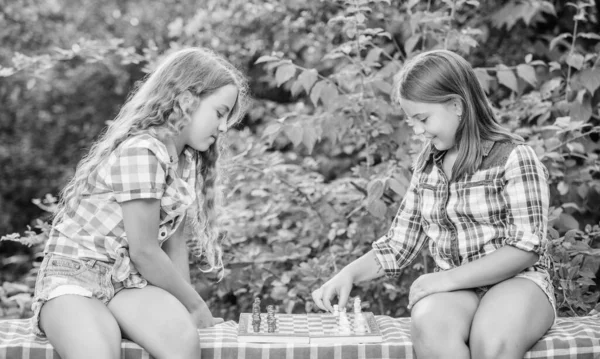 Спортивно-развлекательная концепция. Девочки играют в шахматы. Сестры играют в шахматы. Умные дети. Раннее детство. Интеллектуальная игра. Думай лучше. Дети играют в шахматы на природе — стоковое фото