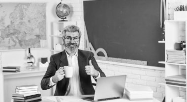 İyi iş için iyi bir içki. Bardaklı sakallı adam, başparmağını uzat. Kıdemli öğretmen sınıfta kahve içer. Sıcak kafein içeceği. Lezzetli bir içecek tarifi. Okul tatili. Mola zamanı. Öğrenme ve öğretme