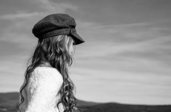 Uzun kıvırcık saçlı genç kız gökyüzü arka planında modaya uygun bir şapka giyiyor. — Stok fotoğraf