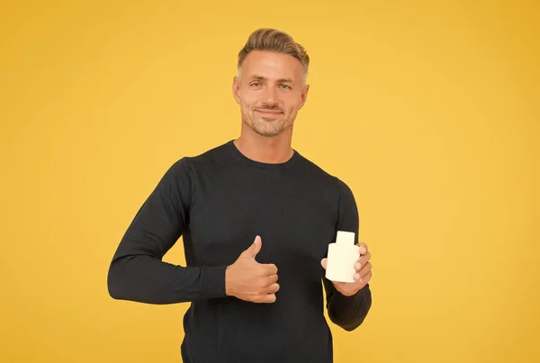 Счастливый белый парень со стильными волосами в непринужденном стиле показать большие пальцы руки жеста держа одеколон бутылку желтый фон, одобрение — стоковое фото