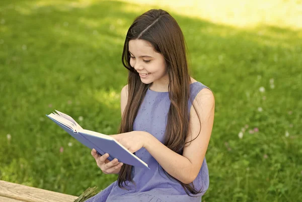 Читайте і подивіться, які чудові речі в книзі. Щаслива дівчина читала книжку на лавці парку. Маленький читач влітку на відкритому повітрі. Прочитай весело. Фантазія та фантастика. Література та поезія. Народжені читати — стокове фото
