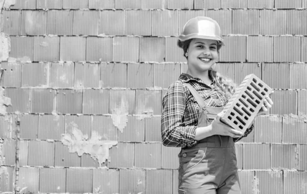 벽돌을 쥐고 있는 십 대 소녀. 벽돌을 가진 작은 건축가입니다. 아이는 엔지니어입니다. 미래의 집을 짓는 거지. 행복 한 어린 시절. 아이들은 보호용 헬멧을 씁니다. 건축 현장에서 머리를 보호하는 일 — 스톡 사진