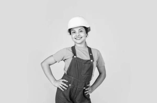Assistent. Portret van een klein meisje met een harde hoed. Meisje met een harde hoed speelt in de werkplaats. Bescherming en veiligheid van kinderen. Een kleine glimlachende bouwer in een helm. Gelukkige jeugd. loopbaanbegeleiding — Stockfoto