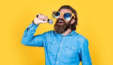 Talan edilmiş. Sakallı adam mikrofonda şarkı söylüyor. Vahşi Kafkas hipster etkinlik yöneticisi. Komik parti gözlükleri. Karaoke ve müzik. Mikrofonlu erkek hoparlör. Sesli. Mutlu gülümseyen olgun adam