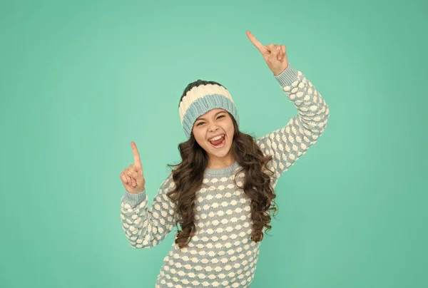 Щаслива дівчина-підліток в трикотажному светрі і капелюсі розважається з піднятими пальцями, творча ідея — стокове фото