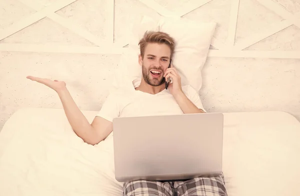 Przystojny człowiek rozmawiać przez telefon oglądanie wideokonferencji online przez komputer w łóżku, nieformalne negocjacje — Zdjęcie stockowe