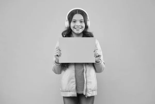 Niño feliz en los auriculares escuchar música. de vuelta a la escuela. niño mantenga el papel vacío para espacio de copia. anuncio de educación en línea. tecnología publicitaria. desarrollo infantil — Foto de Stock