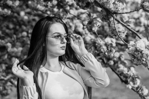 Frau schicke Sonnenbrille in Frühlingsblumen blühen. Mädchen in Kirschblütenblume. Frühjahrsmodenkollektion. Sakura-Baum blüht. Weich und zart. Sakura passt zu ihr. Wunderschöne Blume und weibliche Schönheit — Stockfoto