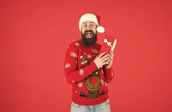 Gelukkig bebaarde man hipster dragen grappig gebreide trui en kerstman hoed en hold huidige doos heeft een idee voor het vieren van kerstfeest, kerstmis winkelen — Stockfoto