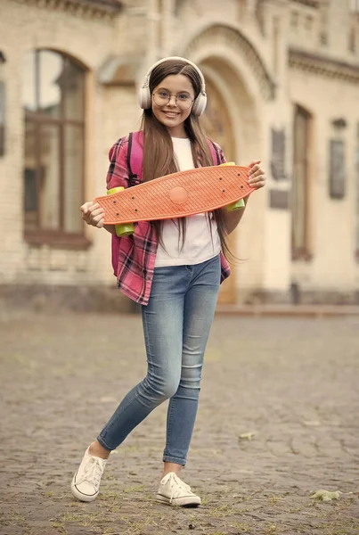 Happy girl słuchać muzyki w nowoczesnych słuchawek posiadających deskorolkę miejskich na zewnątrz, penny board — Zdjęcie stockowe