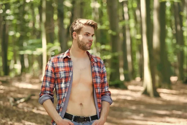 Atractivo y carismático. Hombre sexy de pie en madera en el paisaje natural. Tipo guapo con el torso desnudo sexy en camisa abierta. Vacaciones de verano. Wanderlust y viajar — Foto de Stock