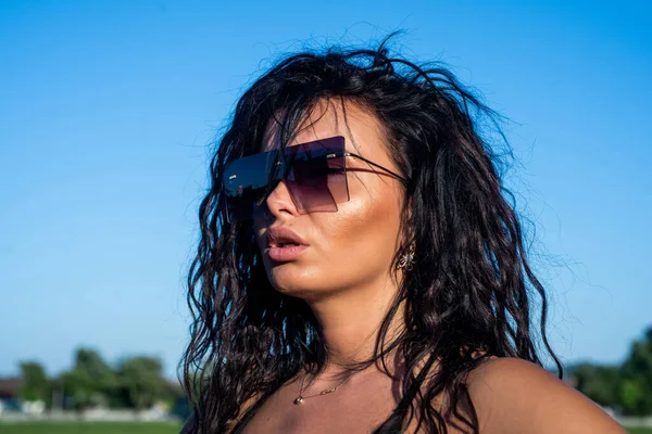 Sexy brunette dame heeft lange krullend haar dragen stijlvolle zonnebril en genieten van de zomer weer buiten, mode en schoonheid — Stockfoto