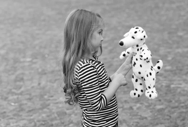 Sérieux petit enfant aux cheveux longs dans un style décontracté jouer avec jouet ami chien à l'extérieur, amitié — Photo