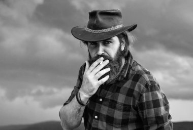 Sakallı olgun bir adam kovboy şapkası takıyor ve sigara içiyor.