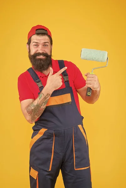 Tersenyum berjenggot pelukis pria pekerja di ketel uap seragam menunjuk jari pada alat rol cat untuk menghadap dinding, memperbaiki — Stok Foto