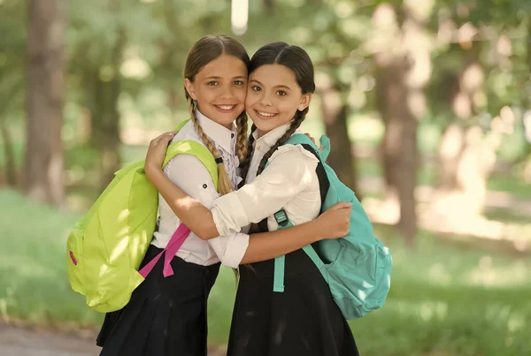 Glada skolkamrater omfamna i formell uniform bär ryggsäckar utomhus, vänskap — Stockfoto