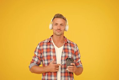 İlham kaynağın. Mutlu adam sarı kahve arkaplanını işaret ediyor. Onaylama ve memnuniyet. Sıcak içecek. Paket kahve. Sabah kahvaltısı. Modern teknoloji. Zevklerde nadir bir deneyim.