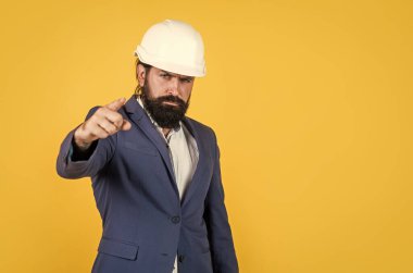Sakallı ciddi bir adam işaret eden sert bir şapka takıyor. Mühendislik Mimari ve bina. Erkek müteahhit koruma için resmi takım elbise ve kask giyiyor. İnşaat projesinde çalışıyorum. Boşluğu kopyala