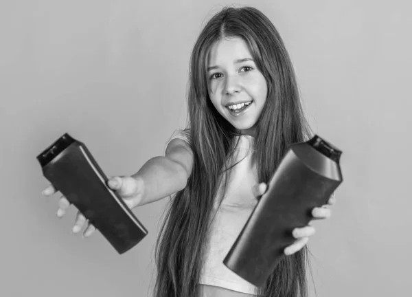 Веселая девочка с длинными прямыми волосами держать кондиционер шампунь или гель бутылку, гигиена — стоковое фото