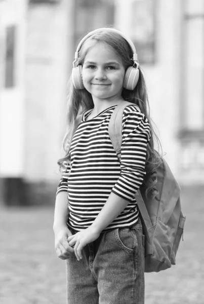 Boldog gyermek hordozza utazótáska zenét hallgatni a modern fejhallgató visel alkalmi divat stílusú városi szabadban, életmód — Stock Fotó