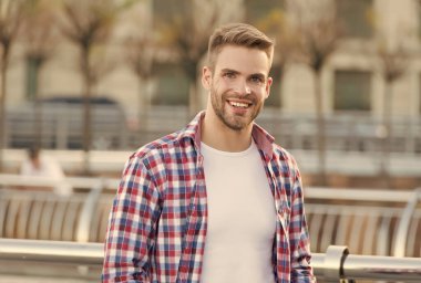 Güzel gülüşü olan, açık havada kareli gömleği olan, traşsız yüzü, erkek modası ve tımarı olan mutlu ve yakışıklı bir adam.