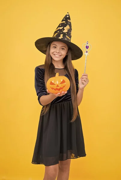 happy girl wear witch hat holding magic wand and pumpkin jack o lantern to create enchantment on halloween, halloween sorcery