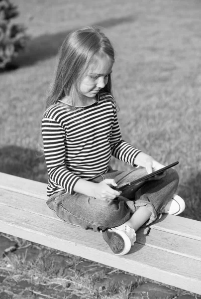 Experimente mudar a maneira como você aprende e joga. Comprimido de uso infantil pequeno sentado no banco do parque. Tecnologia móvel. Vida moderna. Nova tecnologia. Escola online e ensino em casa. Ensino à distância — Fotografia de Stock