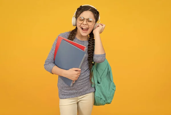 Modernes Studentenmädchen mit Rucksack und Schulmaterial gelber Hintergrund, Playlist-Konzept — Stockfoto