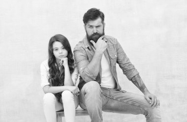 Güzel görünümlü sevimli kız çocuğu ve sıradan moda tarzında sakallı vahşi bir adam tabureye oturur, ciddi.