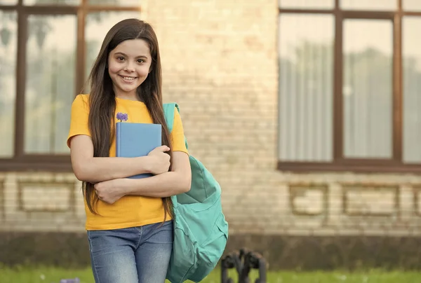 Happy kid with long hair in casual style hold school bag and book for reading, copy space — Stock Fotó