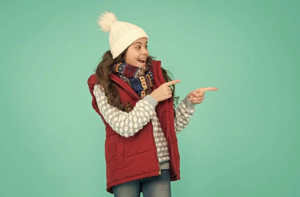 熱衣類広告。幸せな10代の女の子は暖かい服を着る。冬のキッズファッション。編んだ帽子に巻き毛の子供が指を指しています。寒い季節スタイルのクリスマス活動。子供の頃の幸せ — ストック写真