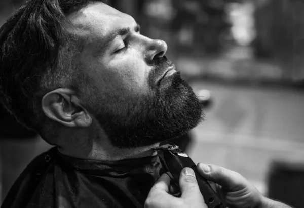 Peinado de pelo y barba. tipo brutal con barbería maestro profesional utilizar la máquina de afeitar eléctrica. hipster. cuidado de peluquero masculino. hombre barbudo en peluquería. belleza y moda. Tocando su barba perfecta — Foto de Stock