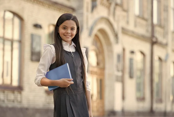 Criança feliz com aparência escolar usar uniforme segurando livro biblioteca ao ar livre, estudo — Fotografia de Stock