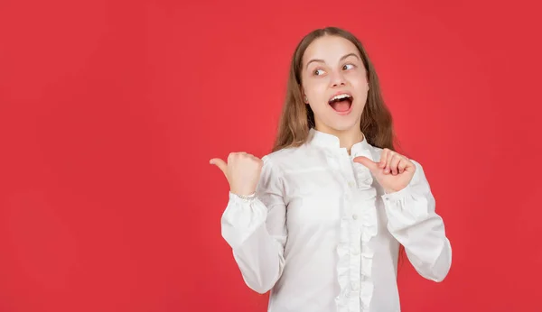 Menina adolescente surpreso na camisa branca apontando o dedo no espaço cópia de fundo vermelho, dirigindo — Fotografia de Stock