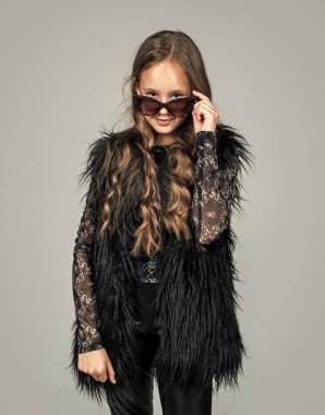 Moda gözlüğü takan şık bir çocuk. Mevsimlik sonbahar modası. Güneş gözlüklü genç kız. Mutlu çocukluk. Güzellik ve moda. Havalı olmak. Çocuğun uzun kıvırcık saçı var.